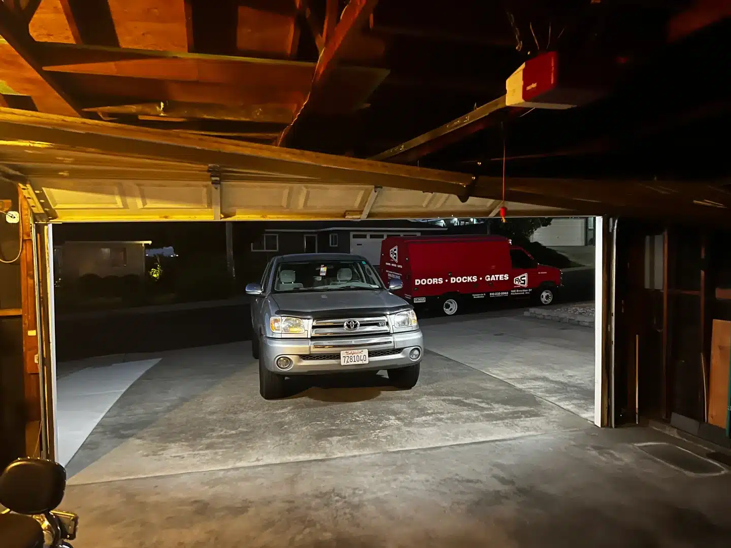 An interior look reveals a crooked garage door stuck half-open over a parked truck at night, demonstrating a high-priority situation requiring emergency garage door repair in Richmond, CA.