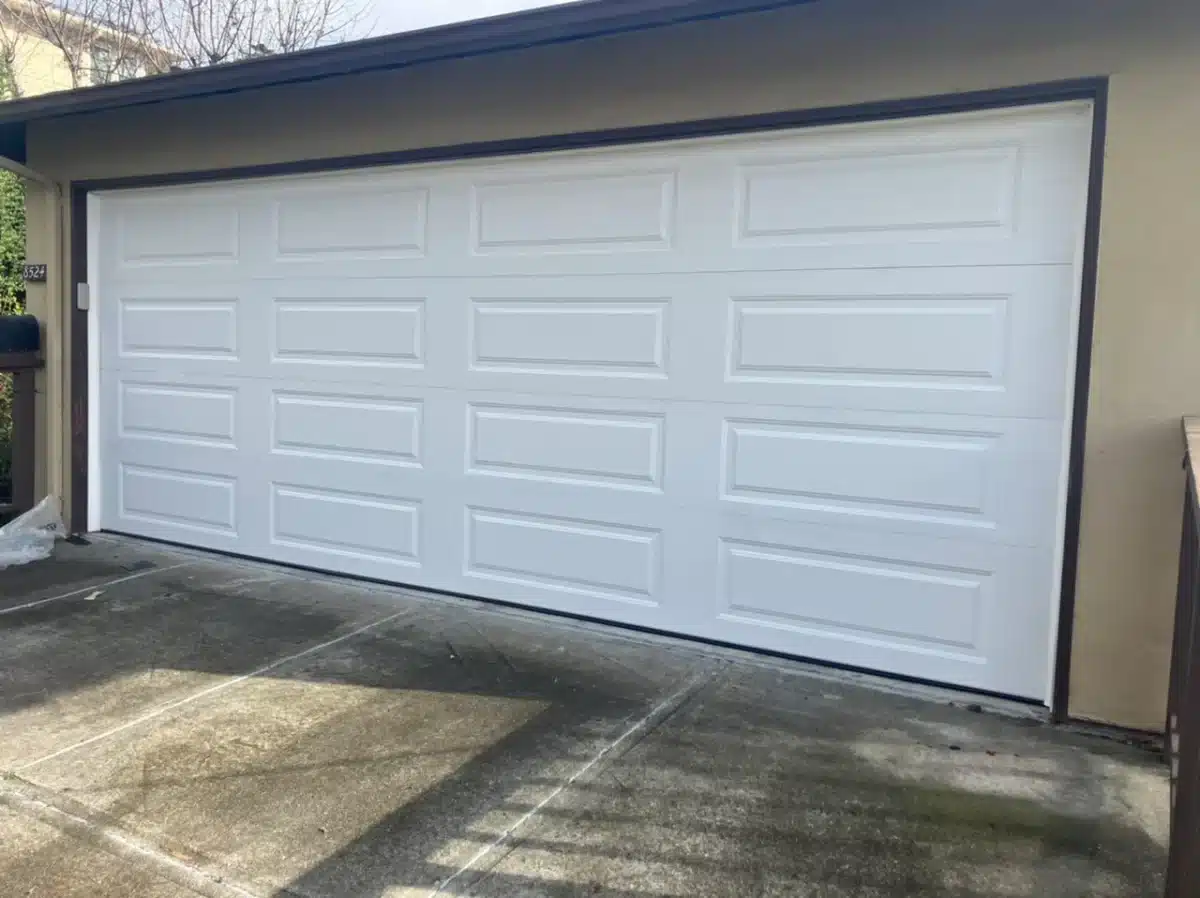 A classic white traditional raised-panel sectional garage door stands cleanly installed on a residential home, providing a perfect example of services from top-rated garage door repair companies near me.