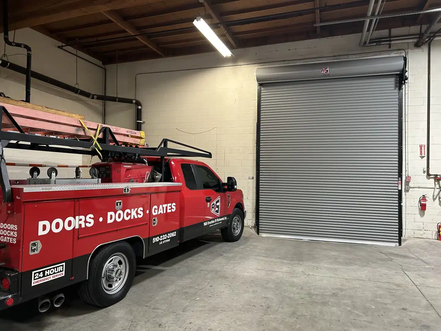 A red service truck is parked inside a warehouse next to a newly serviced industrial roll-up door, highlighting expert maintenance and installation solutions for commercial overhead doors in Richmond.
