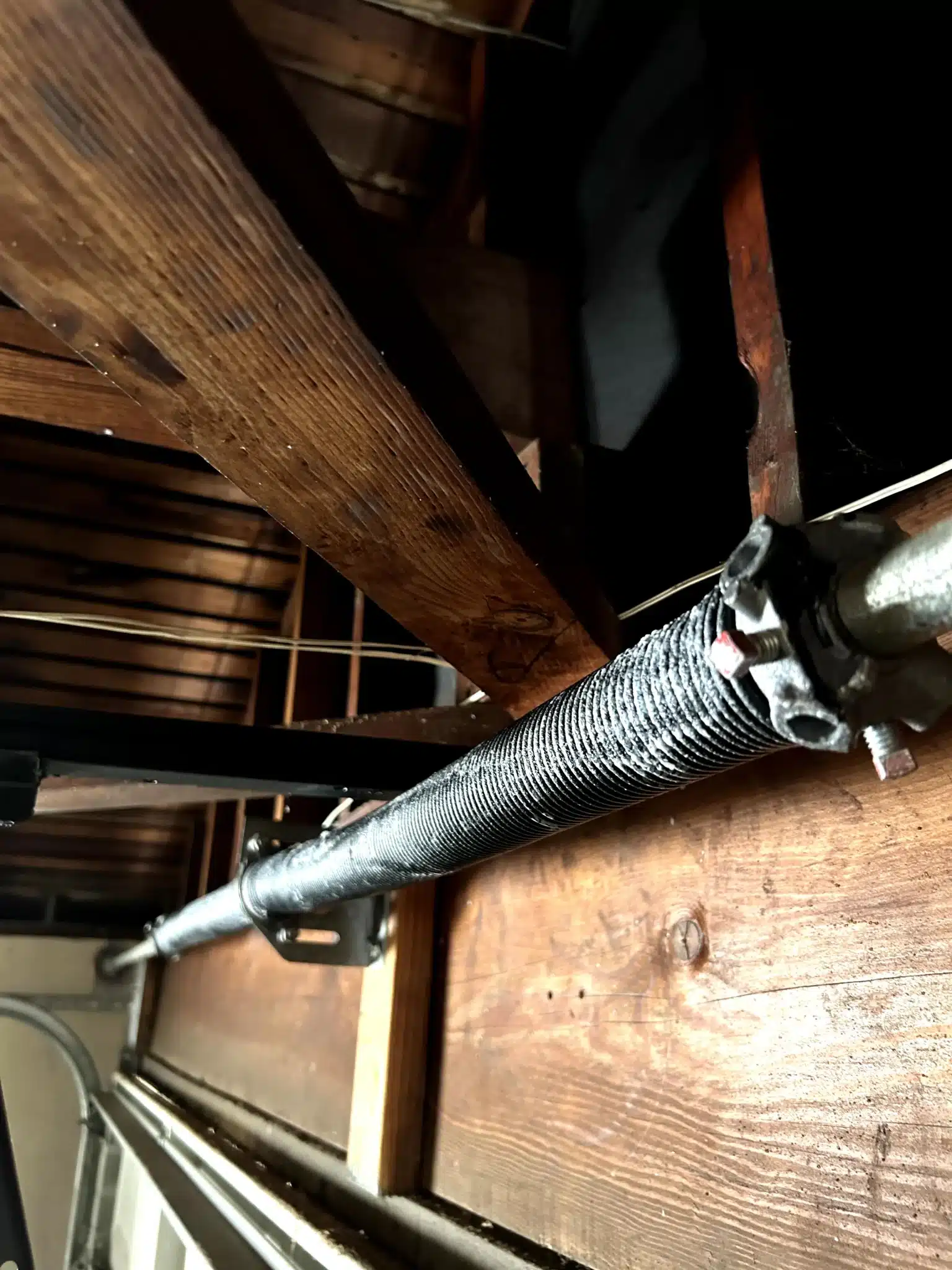 An up-close, interior view reveals a newly installed, solid torsion spring mounted along the metal shaft, demonstrating a completed garage door spring replacement.