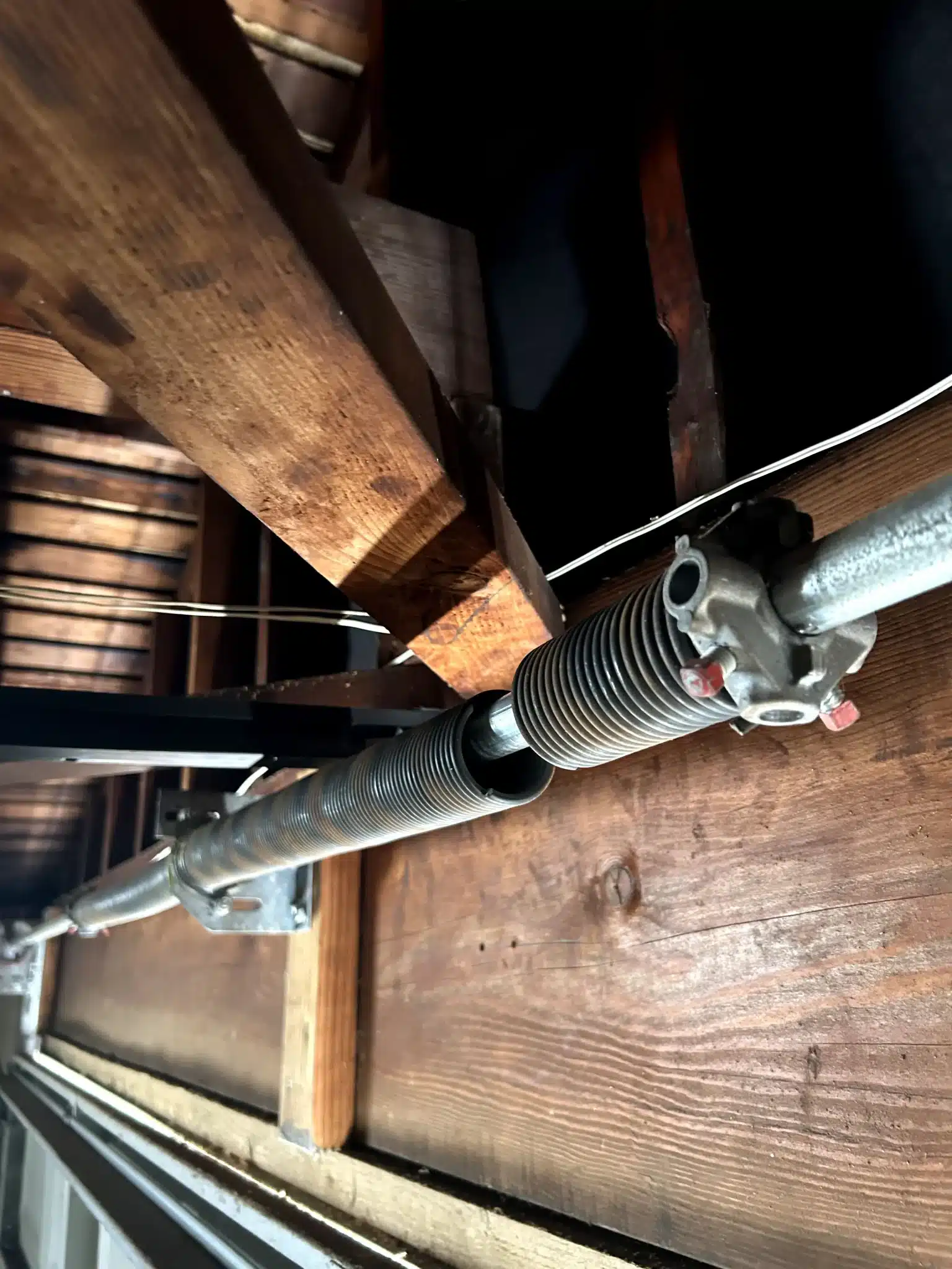 An up-close, interior view reveals a completely broken torsion spring split along the metal shaft, demonstrating a dangerous mechanical failure that poses a major emergency garage door repair safety issue.