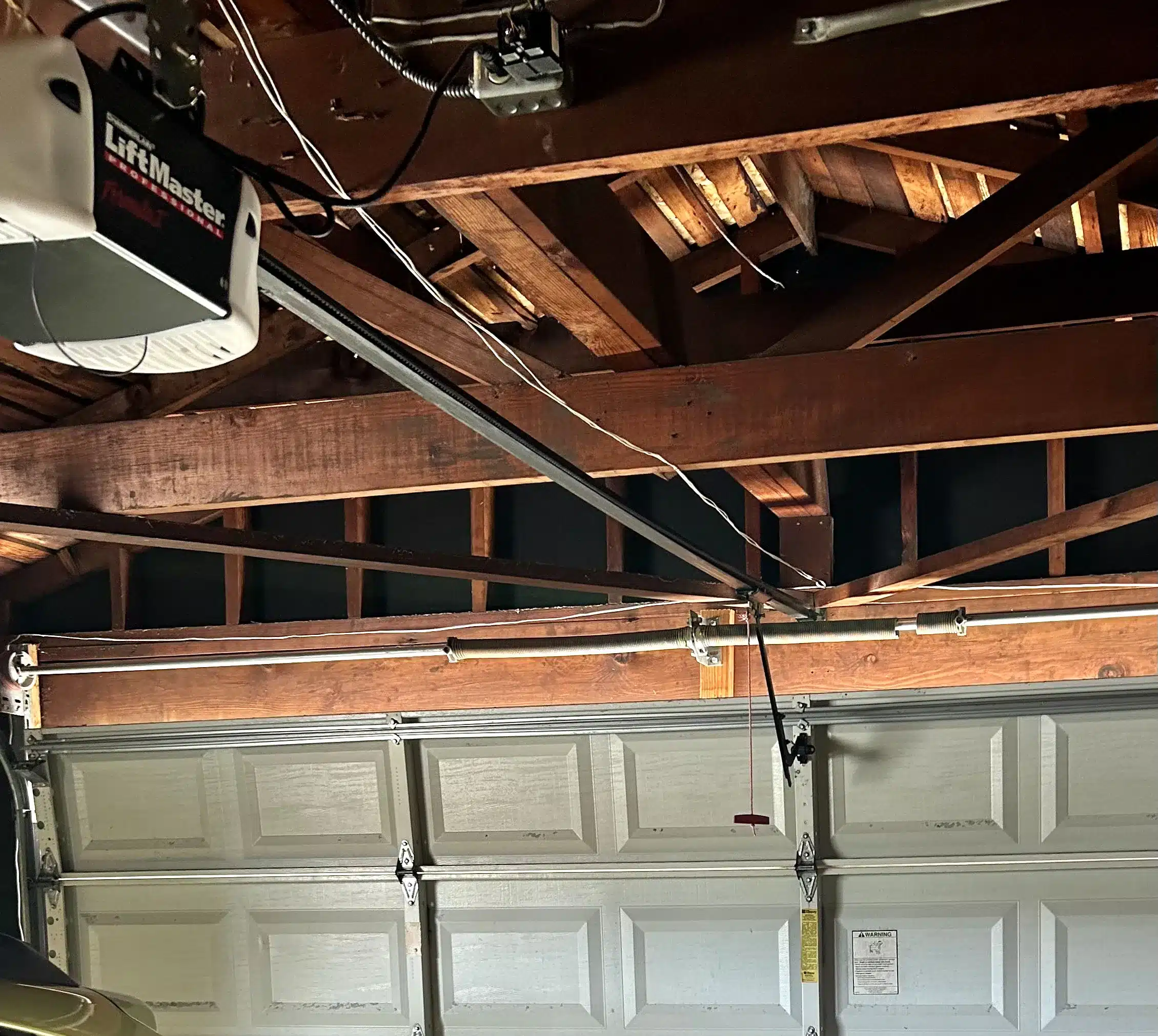 An interior view highlights a LiftMaster opener and an overhead spring system mounted above a closed sectional door, showing a vital component setup when seeking urgent emergency garage door repair near me.