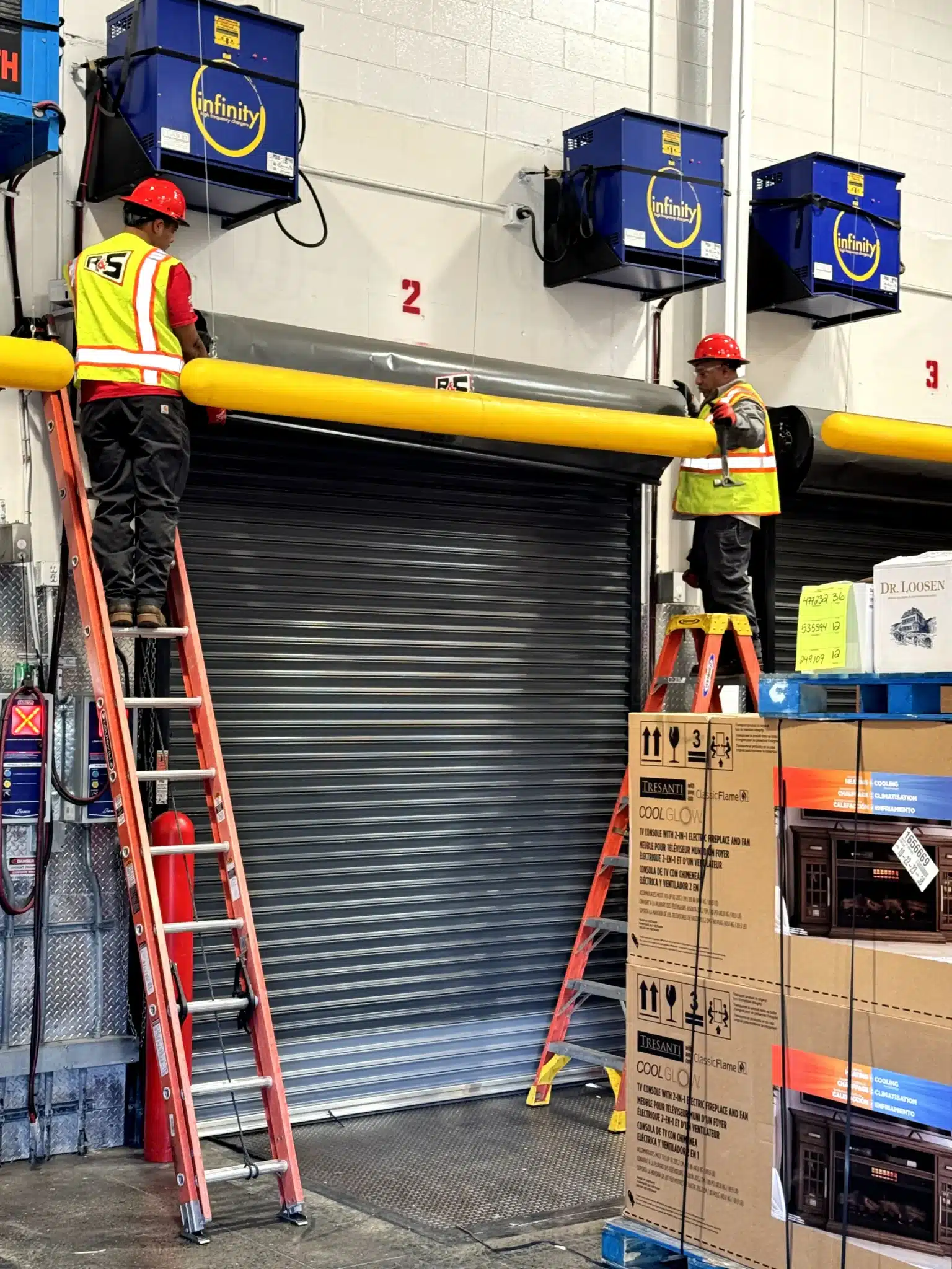 Two technicians wearing safety vests and hard hats work from ladders to service a heavy-duty industrial roll-up dock door, demonstrating the specialized layout and structure found across different types of commercial sectional doors.