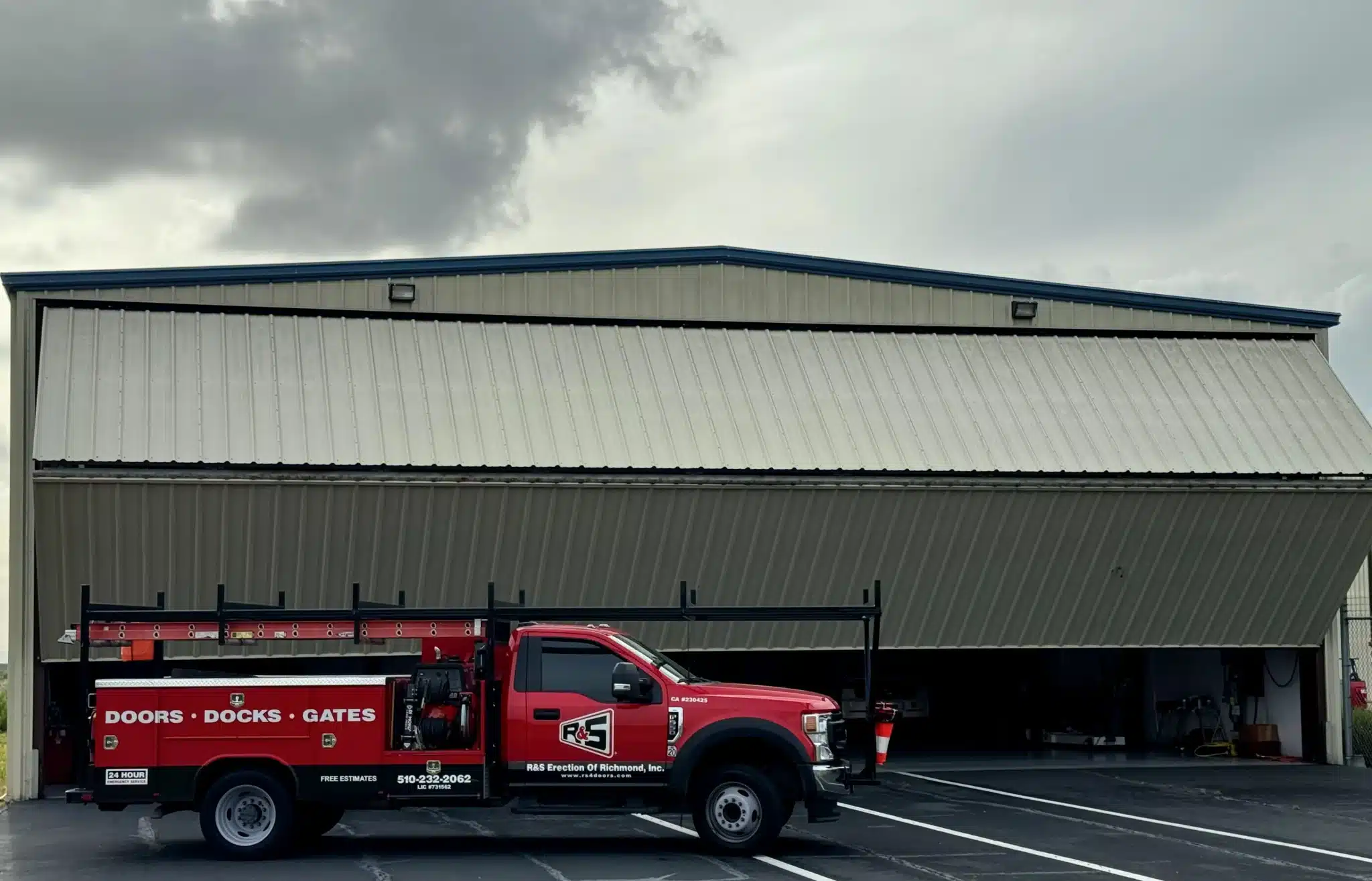 A red service truck is parked in front of a massive hangar facility with a large bifold overhead door system, showcasing professional solutions for energy-efficient commercial sectional doors.