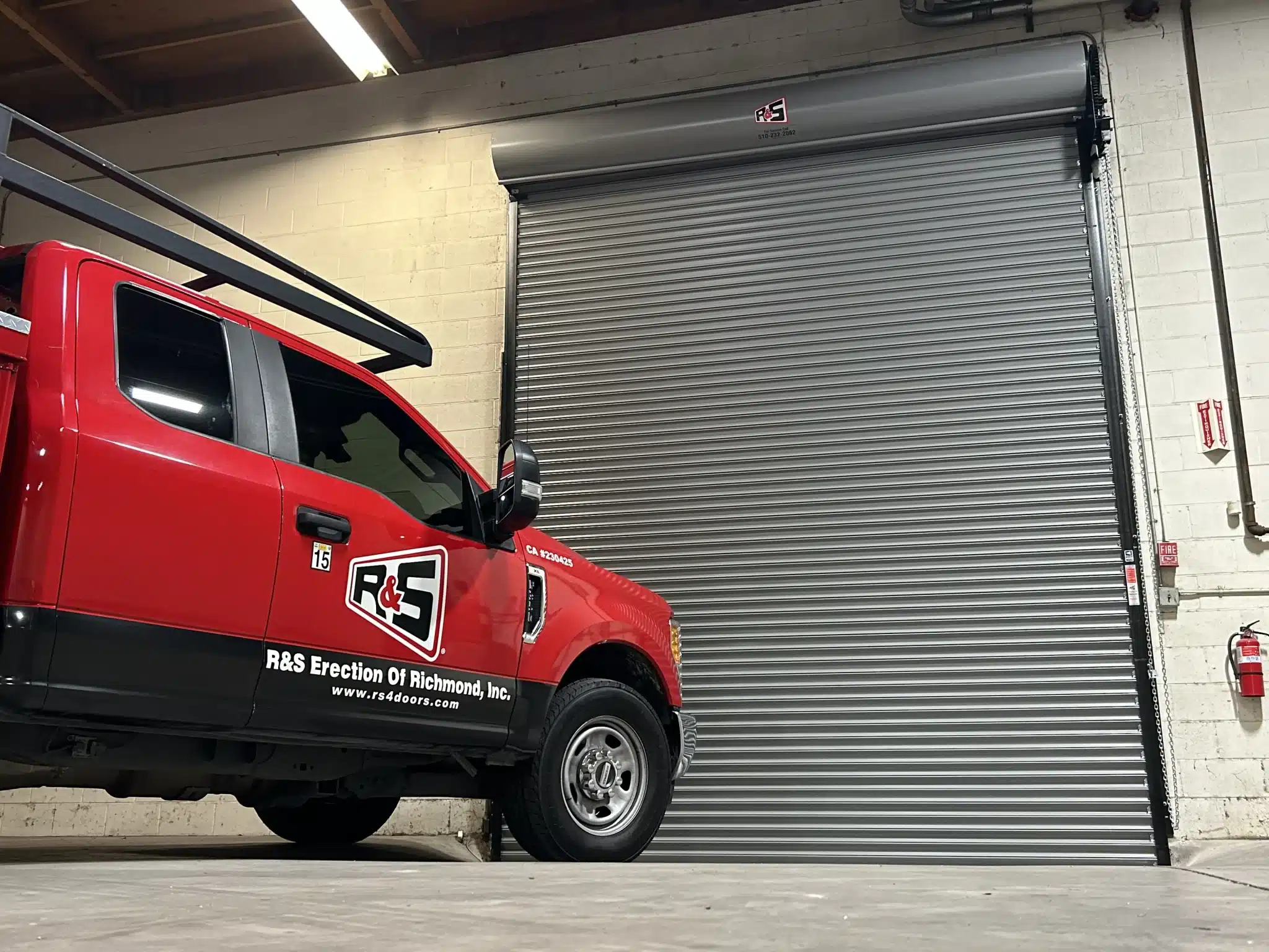 A red service truck parked inside a facility next to a fully closed, pristine gray commercial roll-up door illustrates comprehensive maintenance options for sectional doors.
