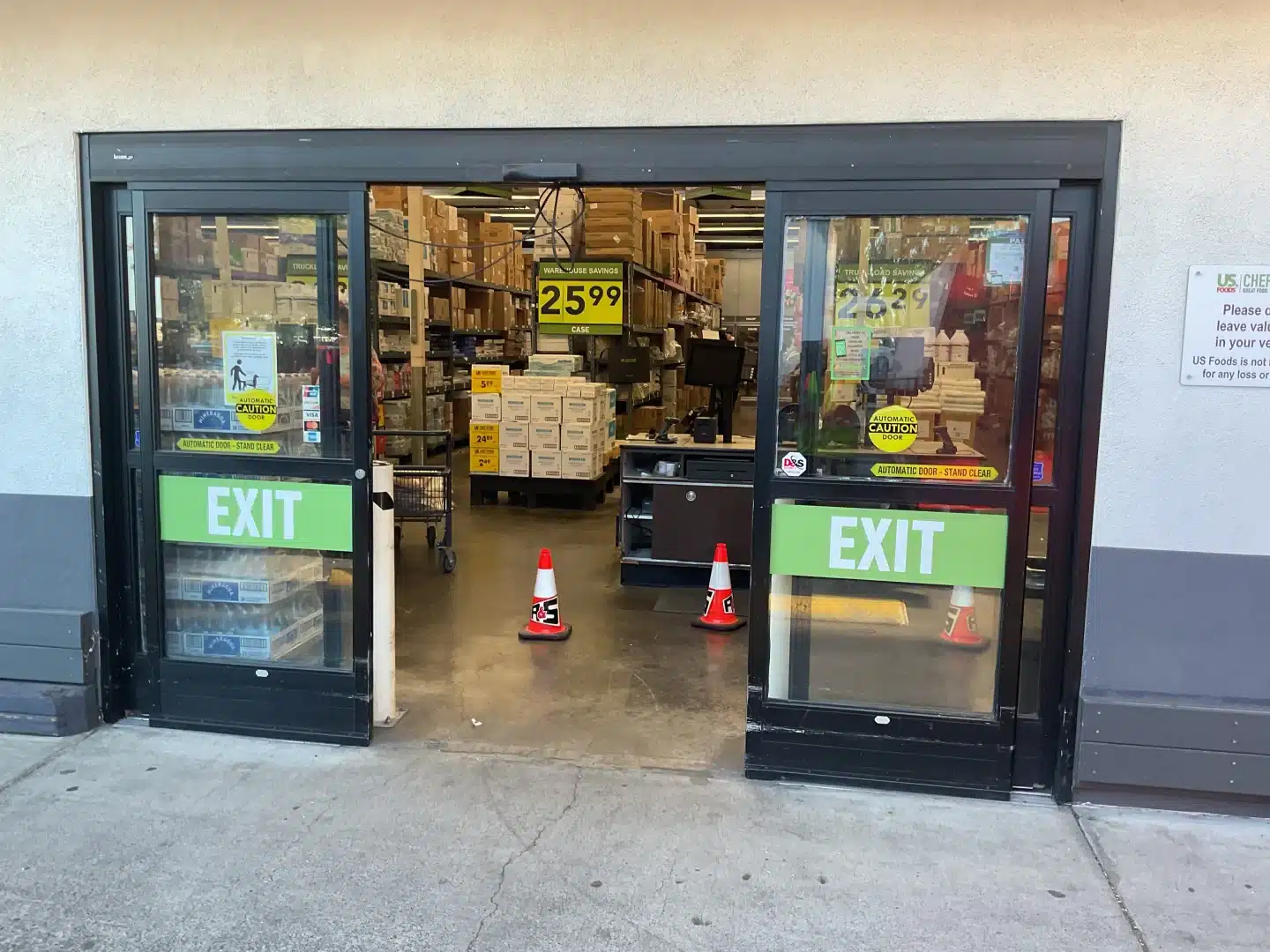 An exterior view looks into a busy retail warehouse environment through a wide, black-framed sliding glass exit entryway, highlighting modern efficiency after an automatic door upgrade.