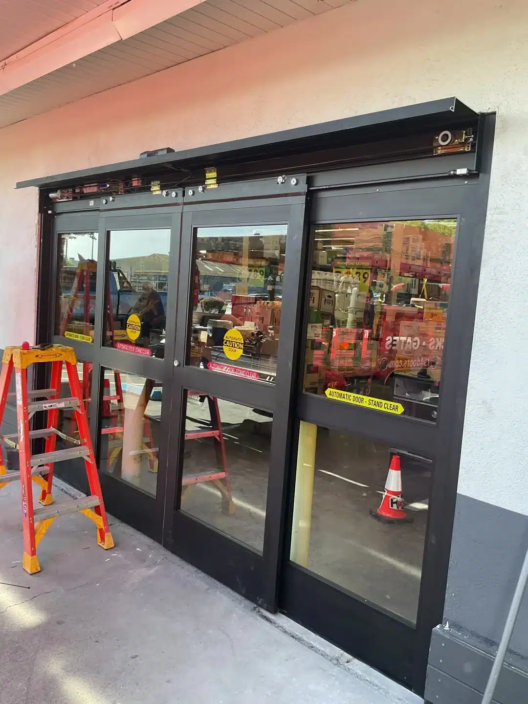 An exterior view shows an open-mechanism sliding glass entrance under service, highlighting the maintenance and structural detail required for reliable automatic commercial doors.