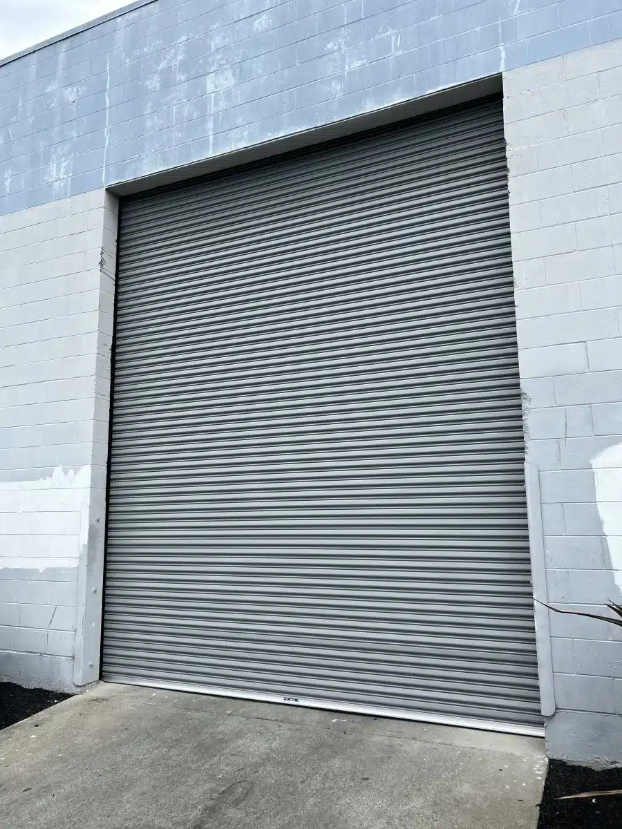 A large, gray corrugated roll-up door is tightly closed within a concrete block wall facade, highlighting robust security and dependable access control for businesses seeking commercial sectional doors near me.