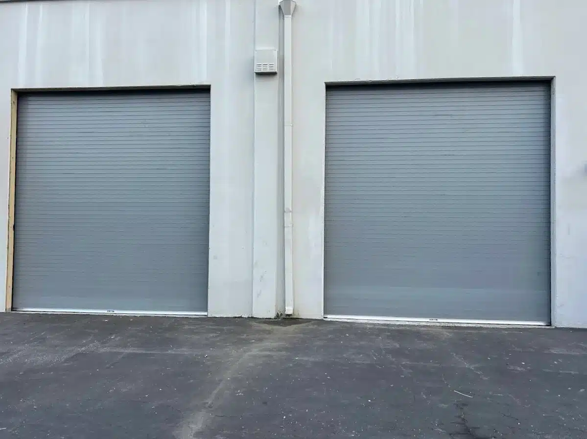 Two gray corrugated roll-up doors sit side-by-side on a commercial building, demonstrating clean lines and enhanced security for modern commercial sectional doors.