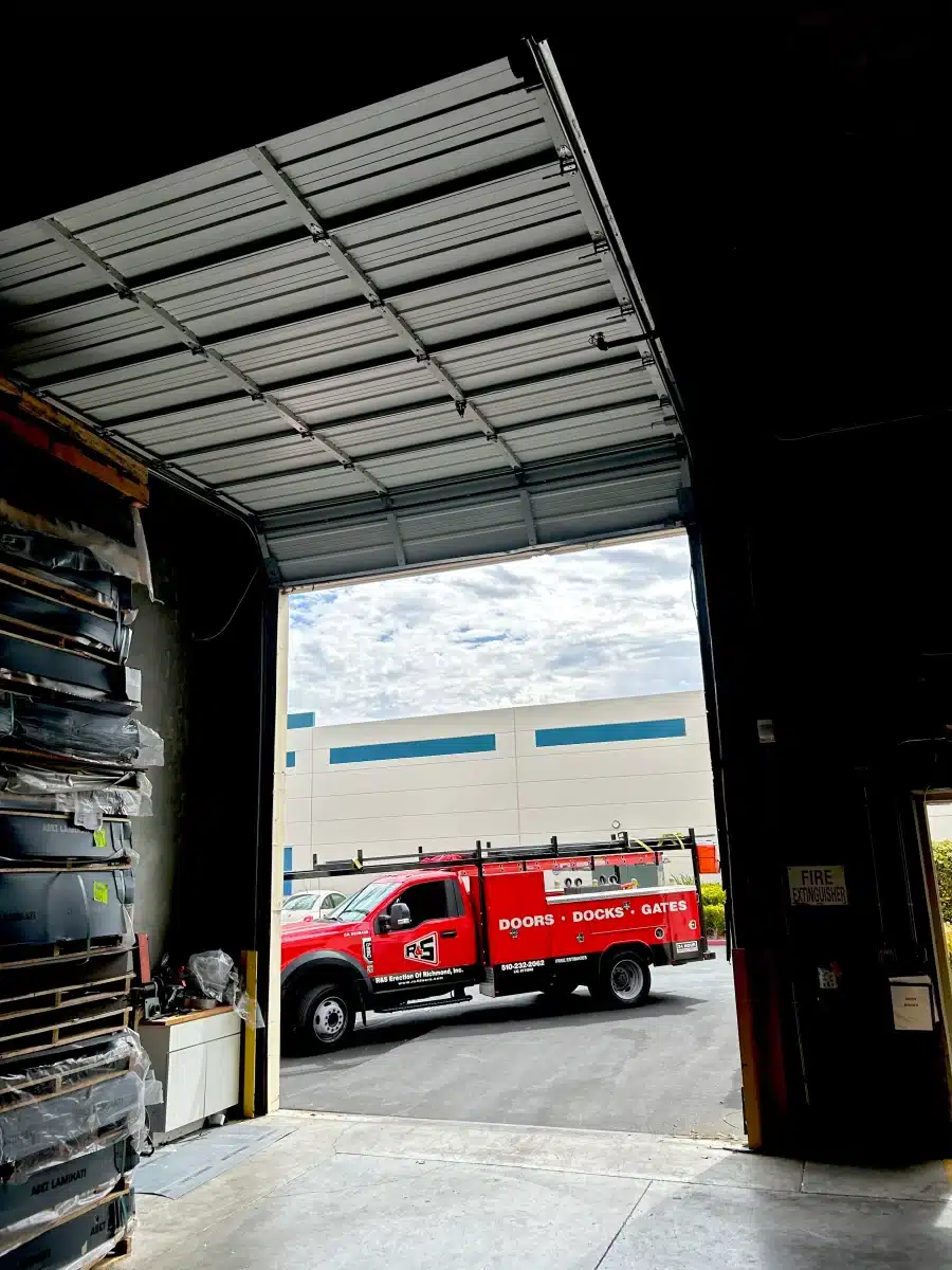 An interior view looks out through a large warehouse bay beneath a fully opened overhead door divided into clean, horizontal sections, illustrating the structure and operation of robust sectional door panels.